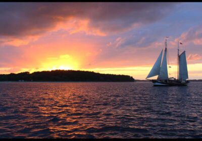 Zeilenin de zonsondergang met een zeilschip