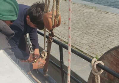 Bemanning en een gast werken aan de tuigage van traditioneel zeilschip Kaat Mossel in de haven
