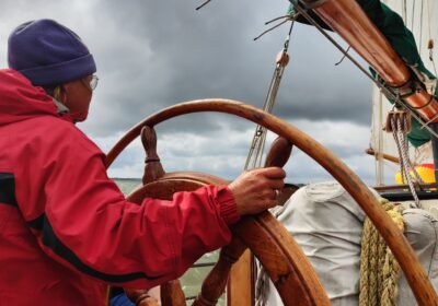 Schipper aan het houten stuurwiel tijdens een zeiltocht met de Kaat Mossel